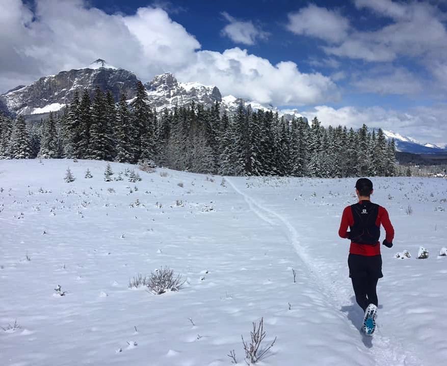 A runner crosses an open field of snow against a mountain backdrop in Canmore, Alberta